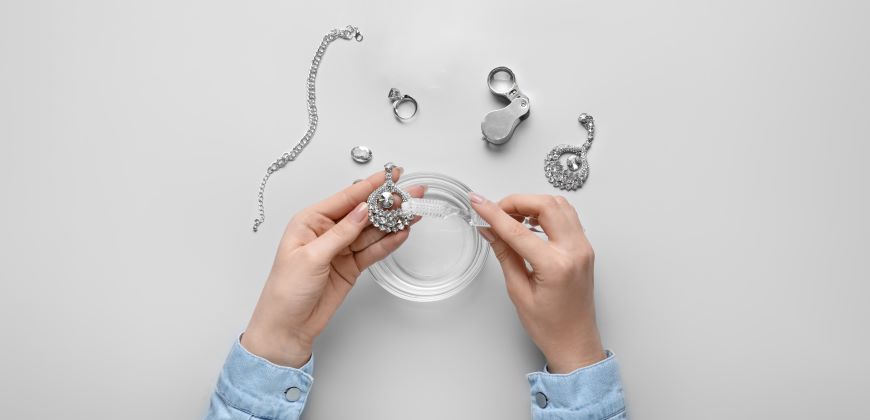 Hands cleaning silver jewelry over a bowl