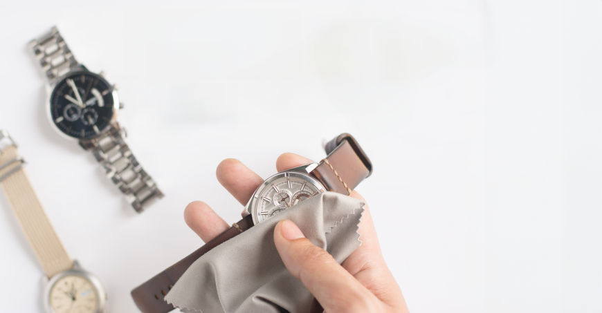 Picture of a hand cleaning a watch and two watches in the background