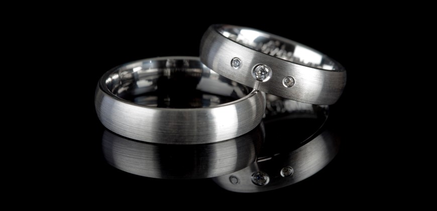 Two men's silver wedding bands on a black background