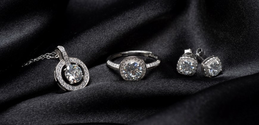 A diamond necklace, ring, and earrings on a black silk background