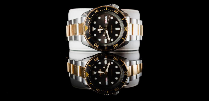A gold, silver, and black watch on a reflective black background