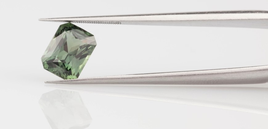 Green sapphire gemstone being held in a tweezers