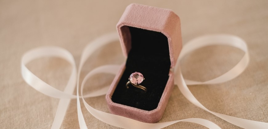 Pink diamond ring in a pink box with ribbon in the background