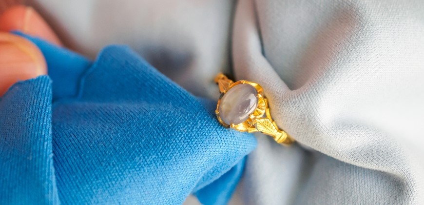 Hands holding a gold gemstone ring between two cloths