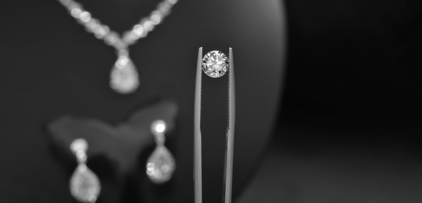 Diamond in a tweezer with a diamond necklace and earrings in the background