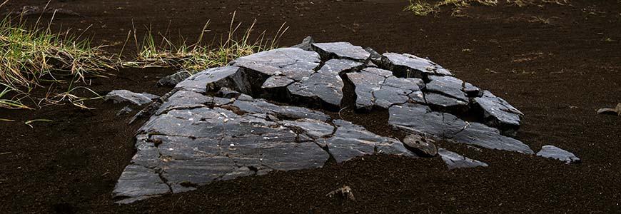 large flat obsidian rock in the middle of a field near a volcano