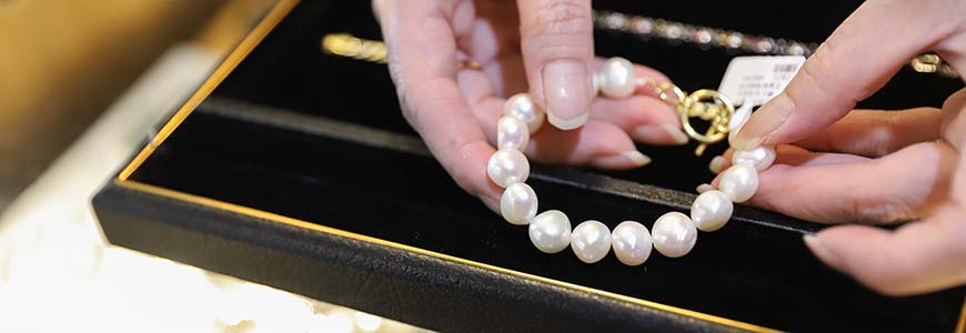 woman's hands pulling pearl necklace out of a cushioned jewelry box
