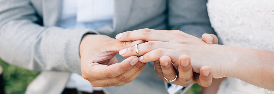 man in grey tuxedo places wedding band on woman in a wedding dress' finger
