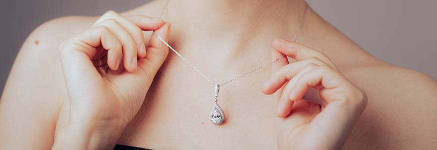 woman holds on to dainty chain necklace featuring a diamond pendant