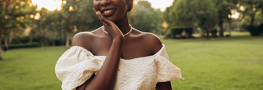 dainty necklace on woman's neck with white puffy off the shoulder dress. woman is standing in a large outdoor space
