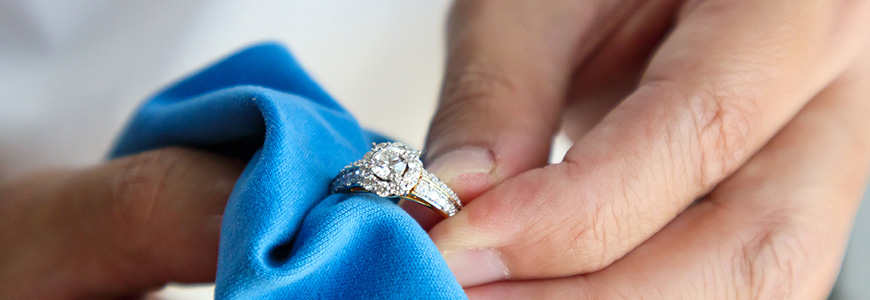 person holding ring while using microfiber cloth to clean it