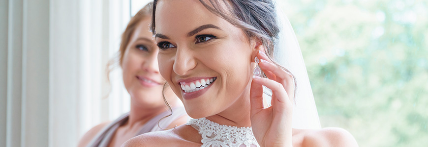 brunette woman with a high neckline wedding dress smiles over shoulder while touching silver earring on ear