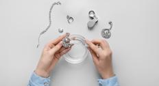 Hands cleaning silver jewelry over a bowl