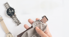 A hand cleaning a watch with a cloth and two other watches in the background