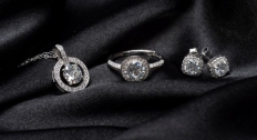 A diamond necklace, ring, and earrings on a black silk background