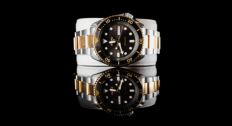 A gold, silver, and black watch on a reflective black background