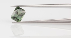 Green sapphire gemstone being held in a tweezers