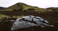 large flat obsidian rock in the middle of a field near a volcano