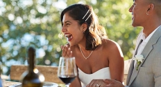 brunette bride with a strapless dress laughs sitting next to husband in a gray tuxedo