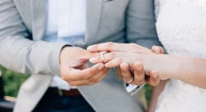 man in grey tuxedo places wedding band on woman in a wedding dress' finger