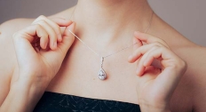 woman holds on to dainty chain necklace featuring a diamond pendant