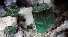 multiple emerald gemstones sit in much larger rock formation 