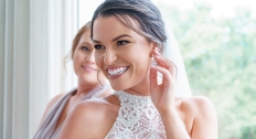 brunette woman with a high neckline wedding dress smiles over shoulder while touching silver earring on ear